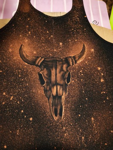 gebeizter Bulle Tanktop im Country-Stil mit dem Bild eines Rinderschädels.
Auf der Rückseite befindet sich im oberen Bereich eine Feder mit Perlen.