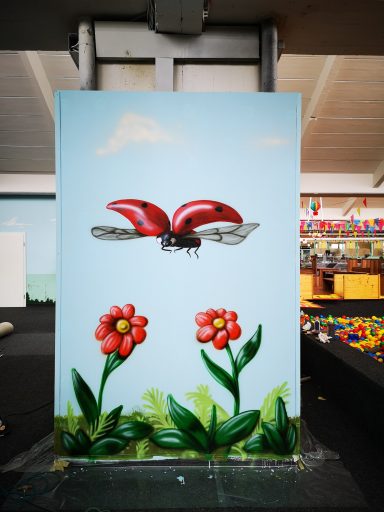 Marienkäfer Bemalte Wand des Indoor Spielplatzes Wölpi. Marienkäfer fliegt über Blumen